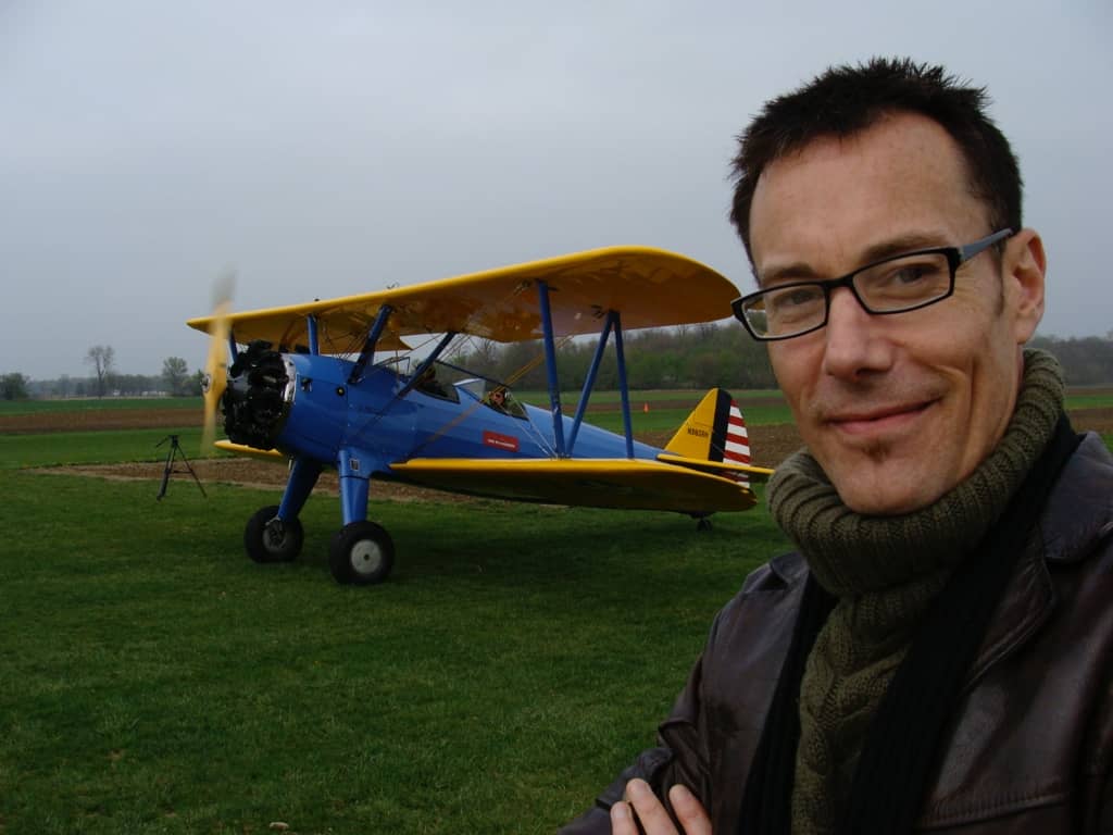 Andrew posing in a field in front of a biplane.